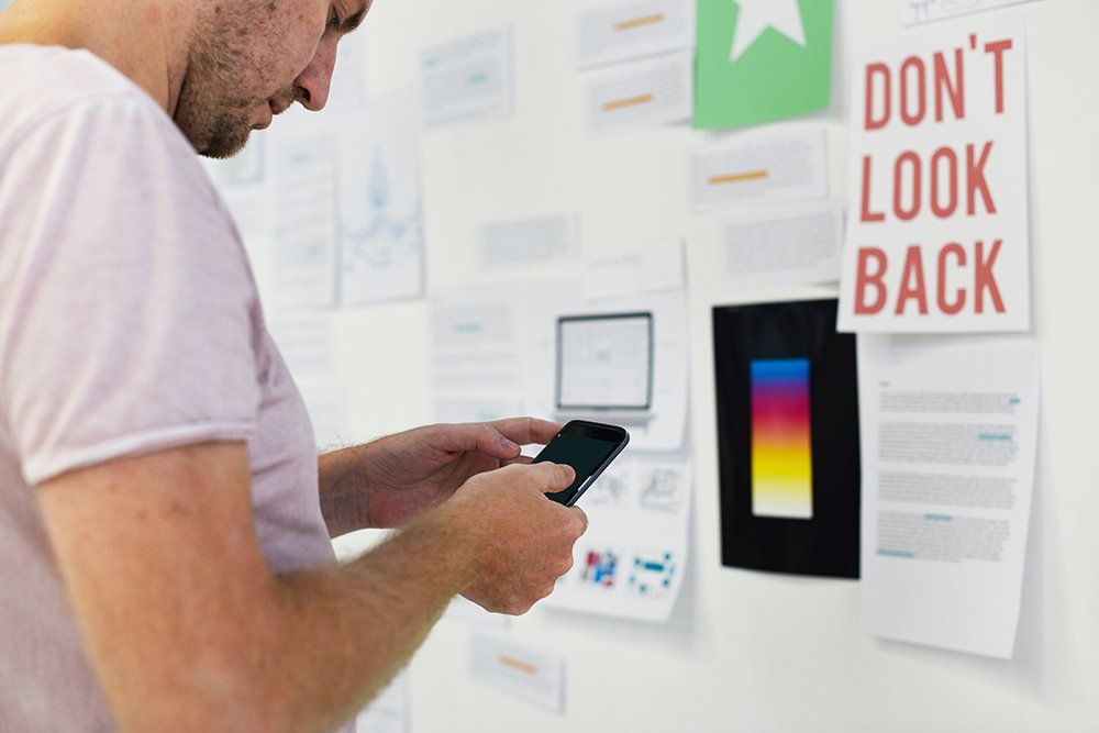 Man using a smartphone to photograph notes and drawings on a white wall in an office setting.